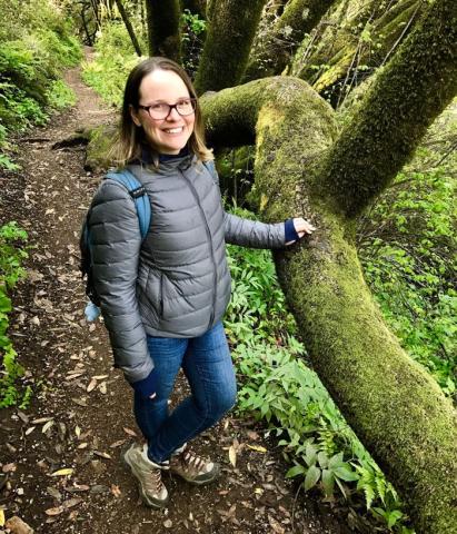 Woman standing in a forest next to a moss covered tree.