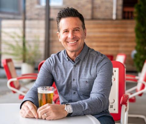 Smilling man sitting at a table with a beer.