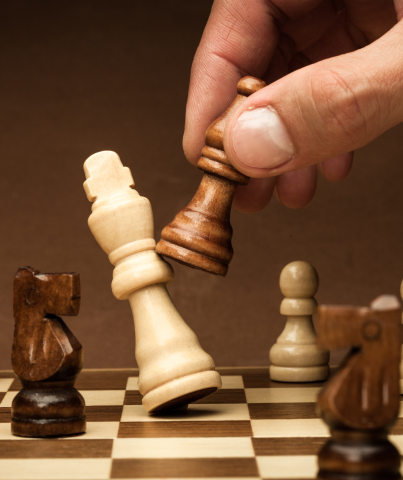 Close up photograph of someone moving a chess piece on a chessboard.