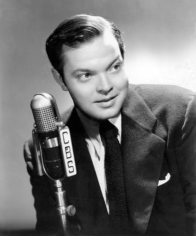 Black and white photograph of Orson Wells speaking into a microphone.