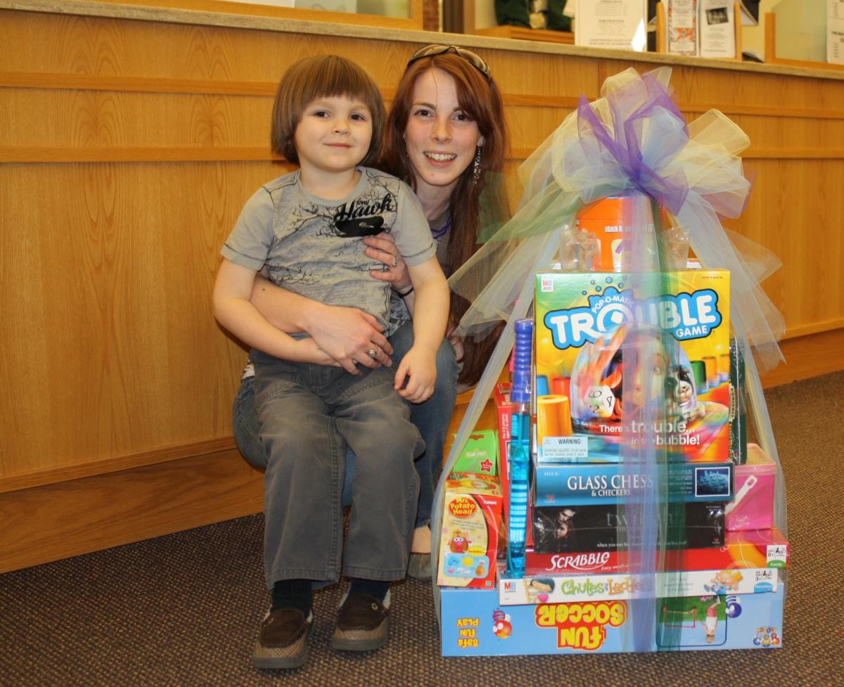 Color photograph of child and adult with a stack of board games won in a raffle.